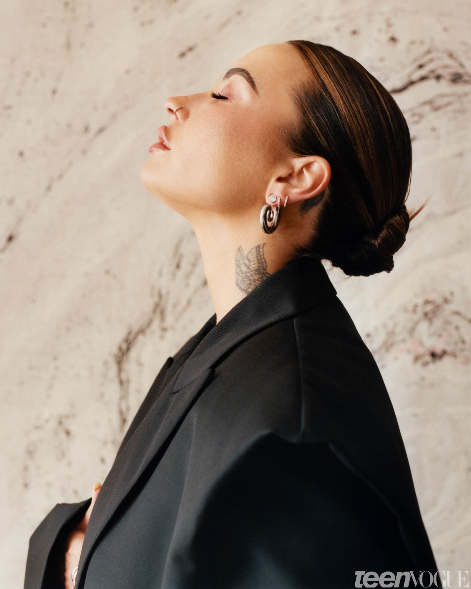 Side profile of Demi eyes closed and a slick back bun wearing the oversized black blazer with shoulder pads.