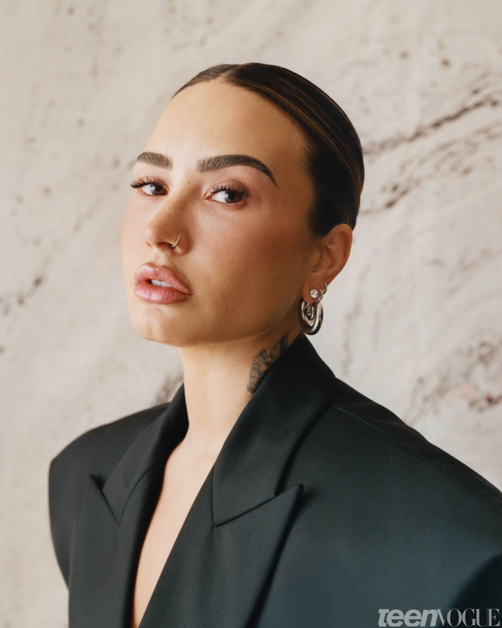 Demi gazing directly at viewer wearing an oversized black blazer with thickly padded shoulders.