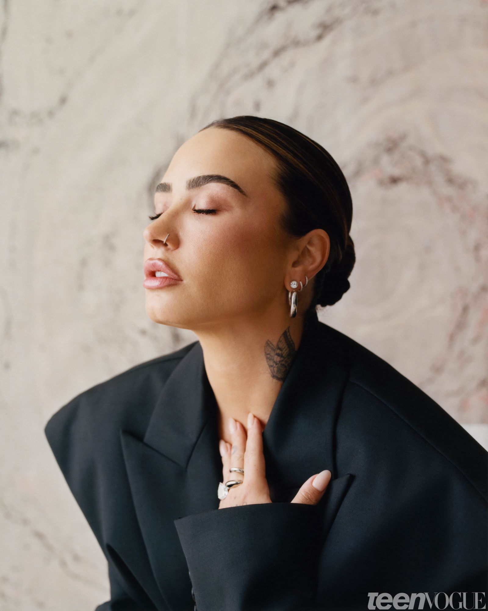 Demi eyes closed facing away from view wearing an oversized black blazer with padded shoulders.