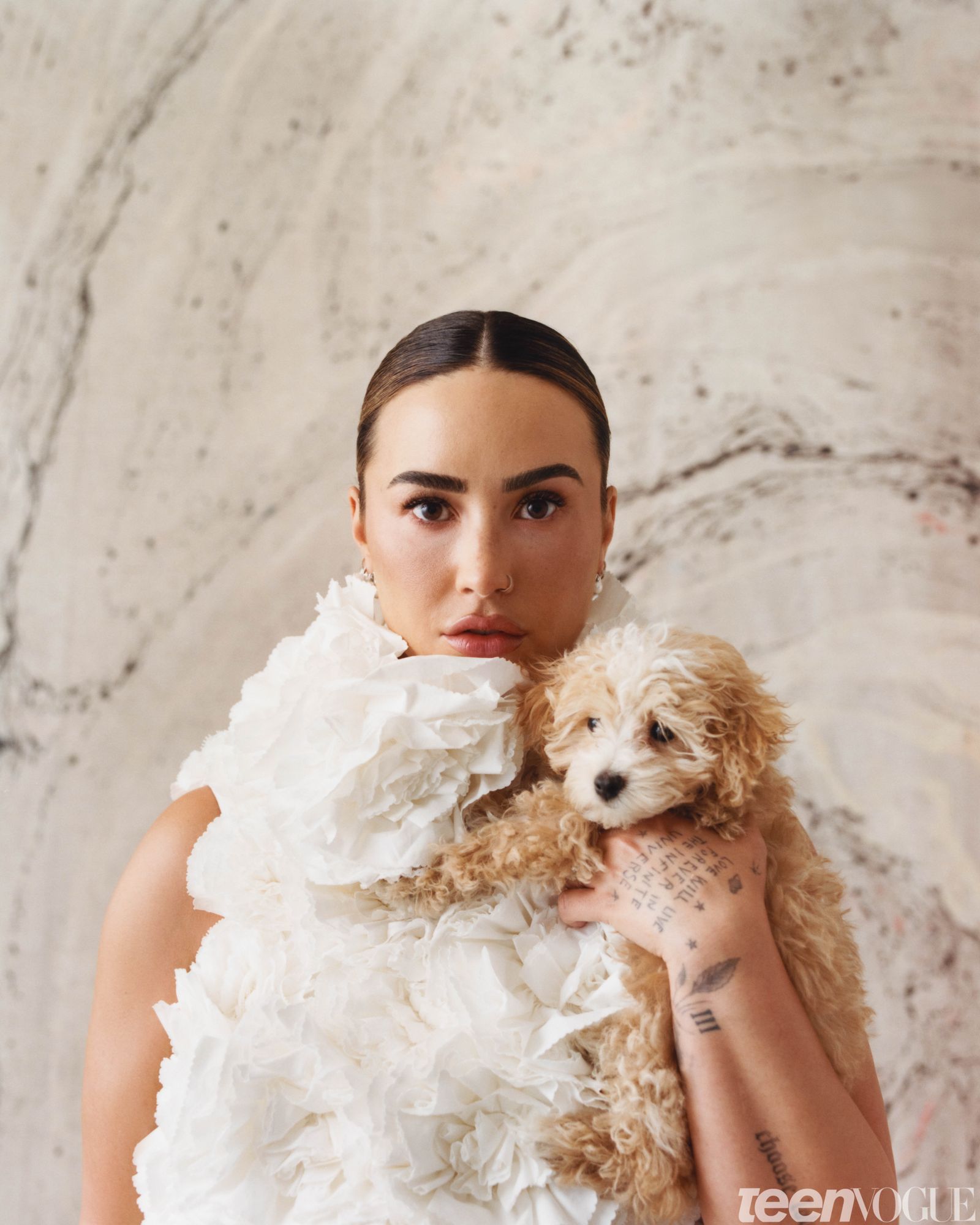 Demi photographed with her puppy named Pickle in a cream dress with white poofy flowers against a marbleprinted backdrop.