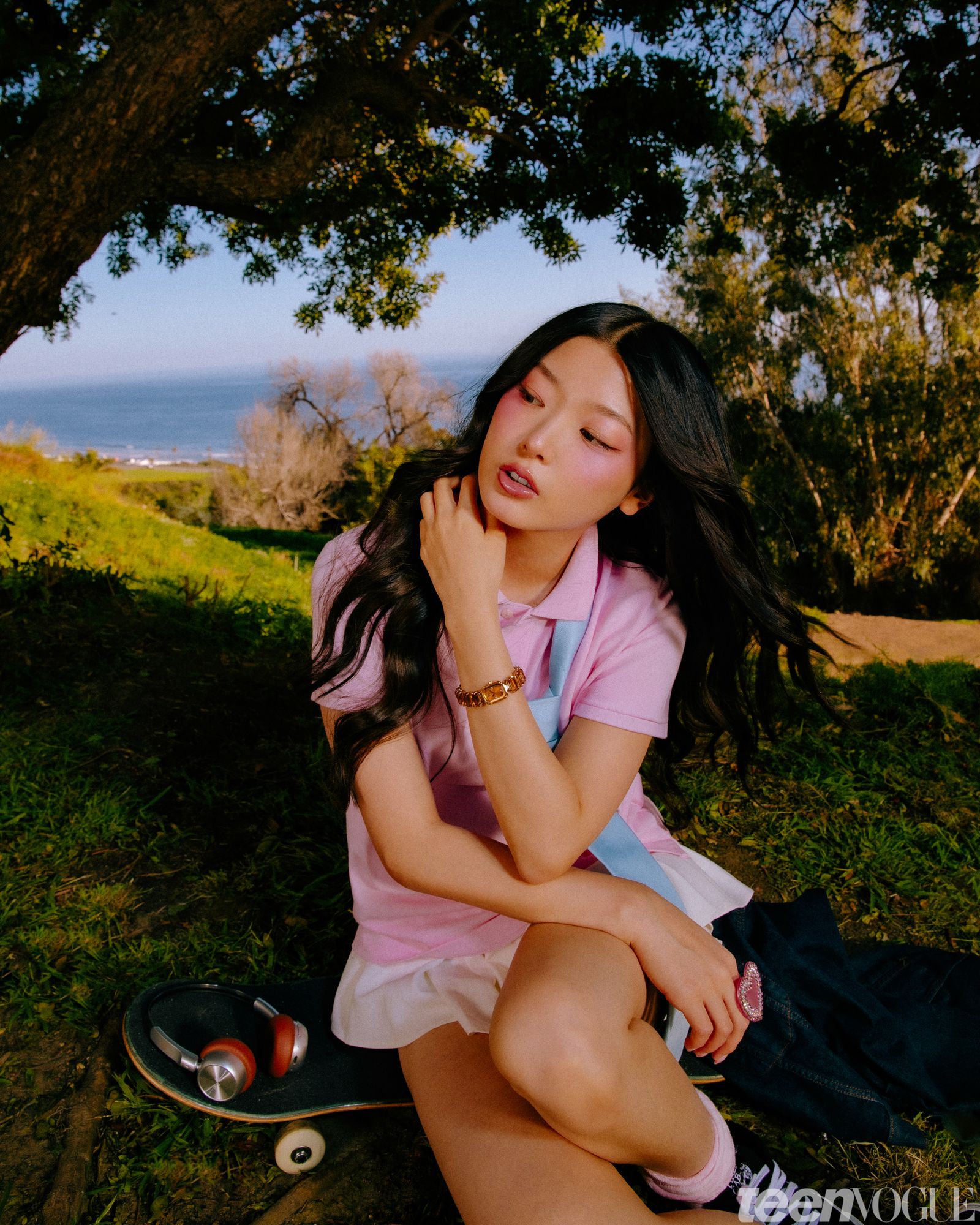 Yoonchae looking away from viewer sitting on a skateboard. She is photographed in the backyard against a tree and the...