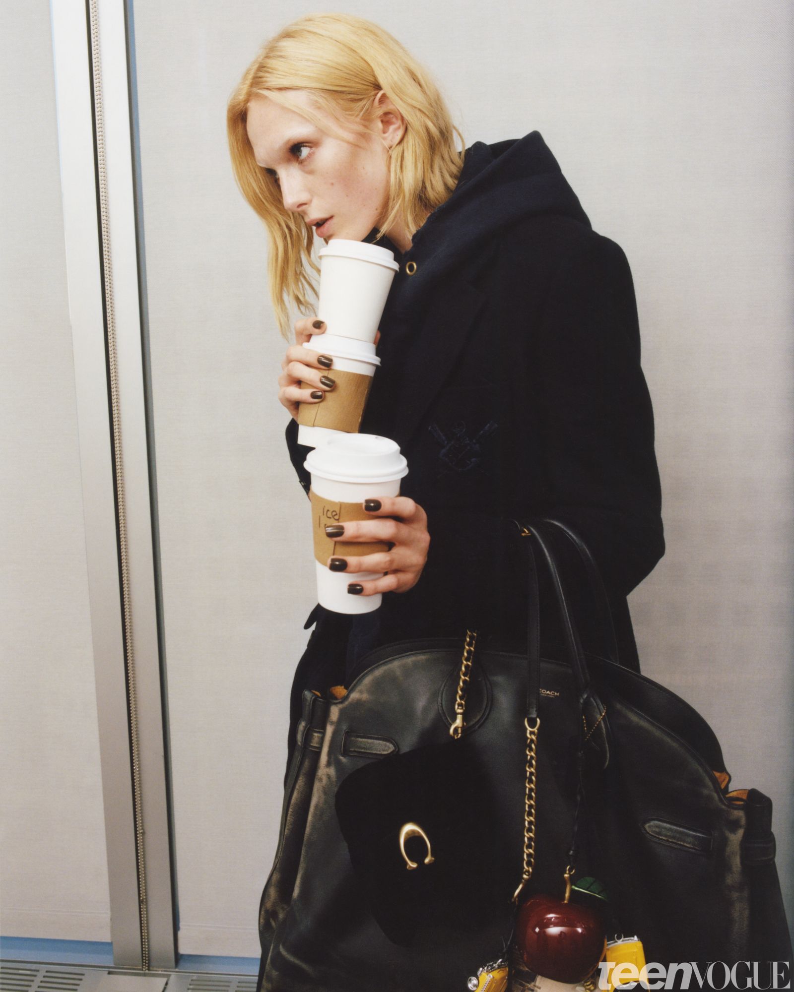 Alex as the Production Assistant. She stacks three coffee cups balancing them just below her chin.
