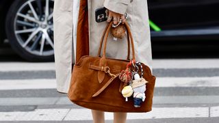 A guest wears red jumper white skirt beige long jacket brown suede Miu Miu aventure bag with aLabubu charm white red...