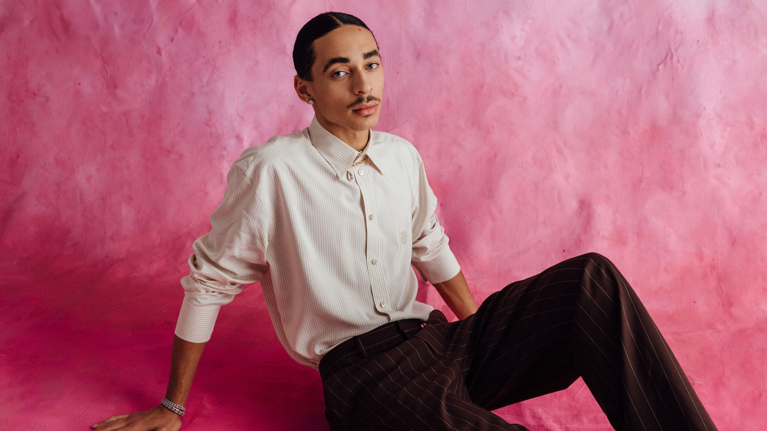 Julez sitting against a pink backdrop.