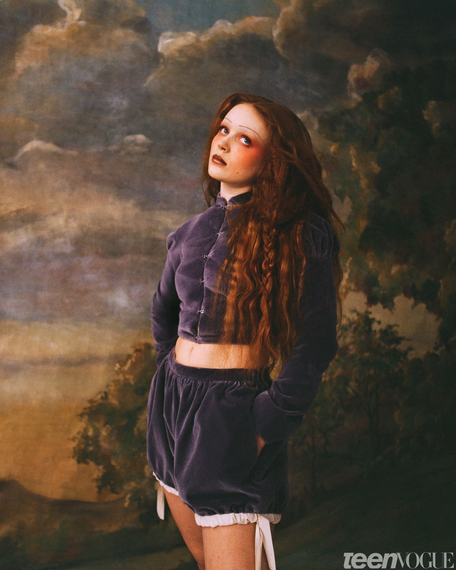Sadie photographed with her hands in her pockets looking up and away from viewer in a matching purple suede jacket and...