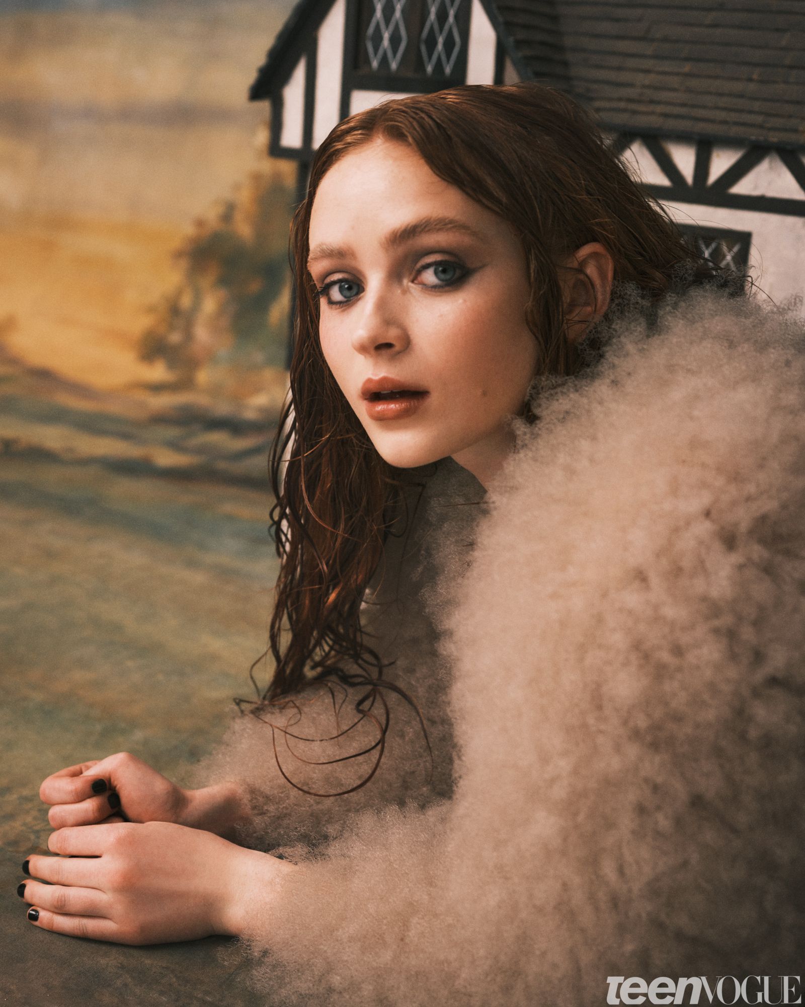 A closeup of Sadie photographed laying down against a painted backdrop and dollhouse behind her.