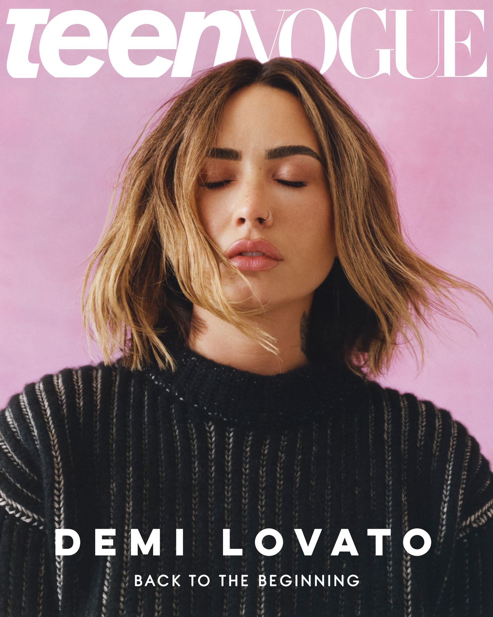 Demi wearing a black knit sweater with her eyes closed and hair blowing against a pink backdrop. Cover reads Demi Lovato...