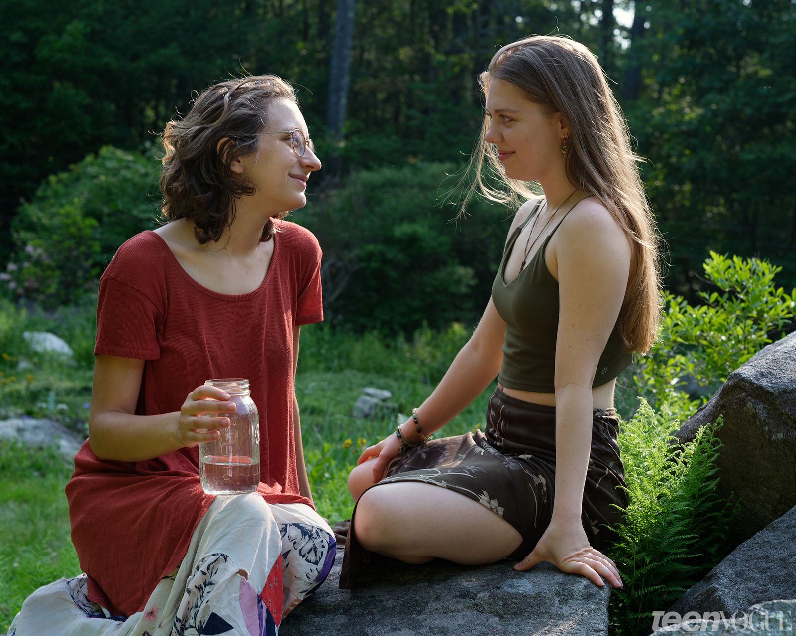 Jo and Madison sitting outside on rocks smiling at each other photographed in Shutesbury Massachusetts. Jo holds a mason...