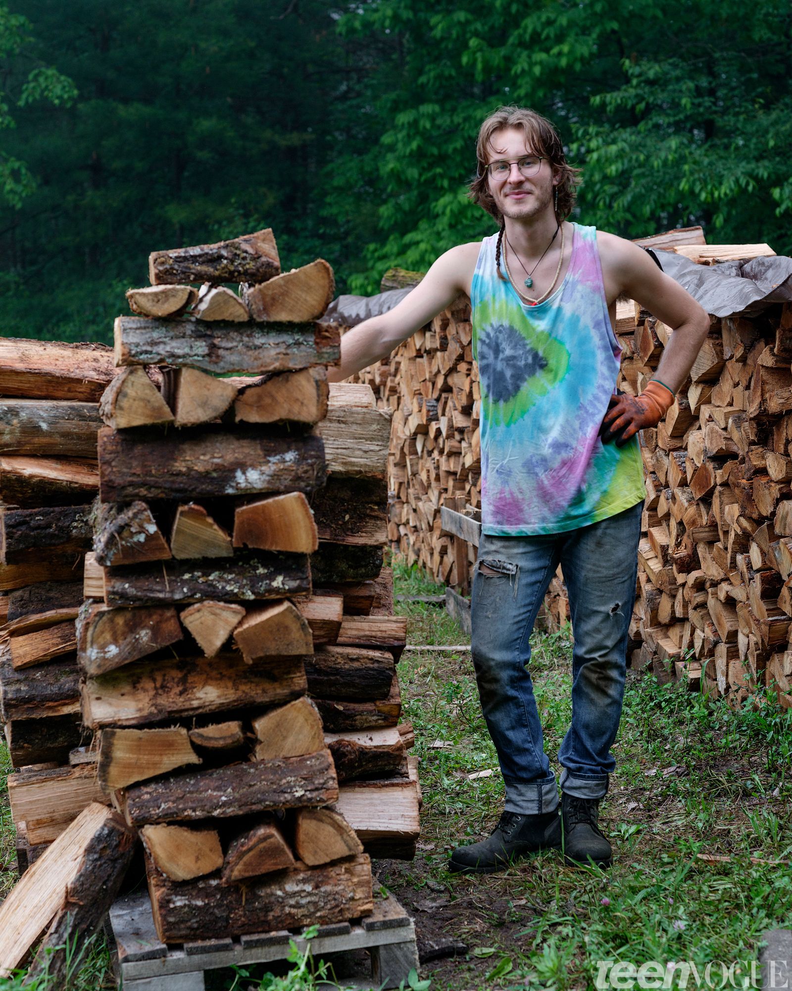 Gabriel Futterman of the Sirius Community photographed in Shutesbury Massachusetts standing next to a tower of wooden logs.