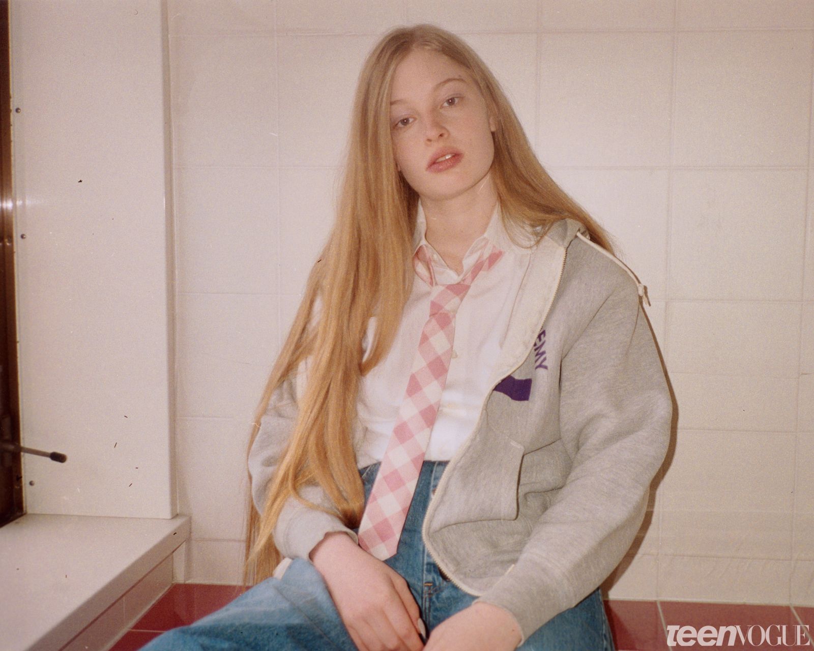 Vivian pictured with flash against a a cream tiled wall. She is wearing a pink and white gingham tie white collared...