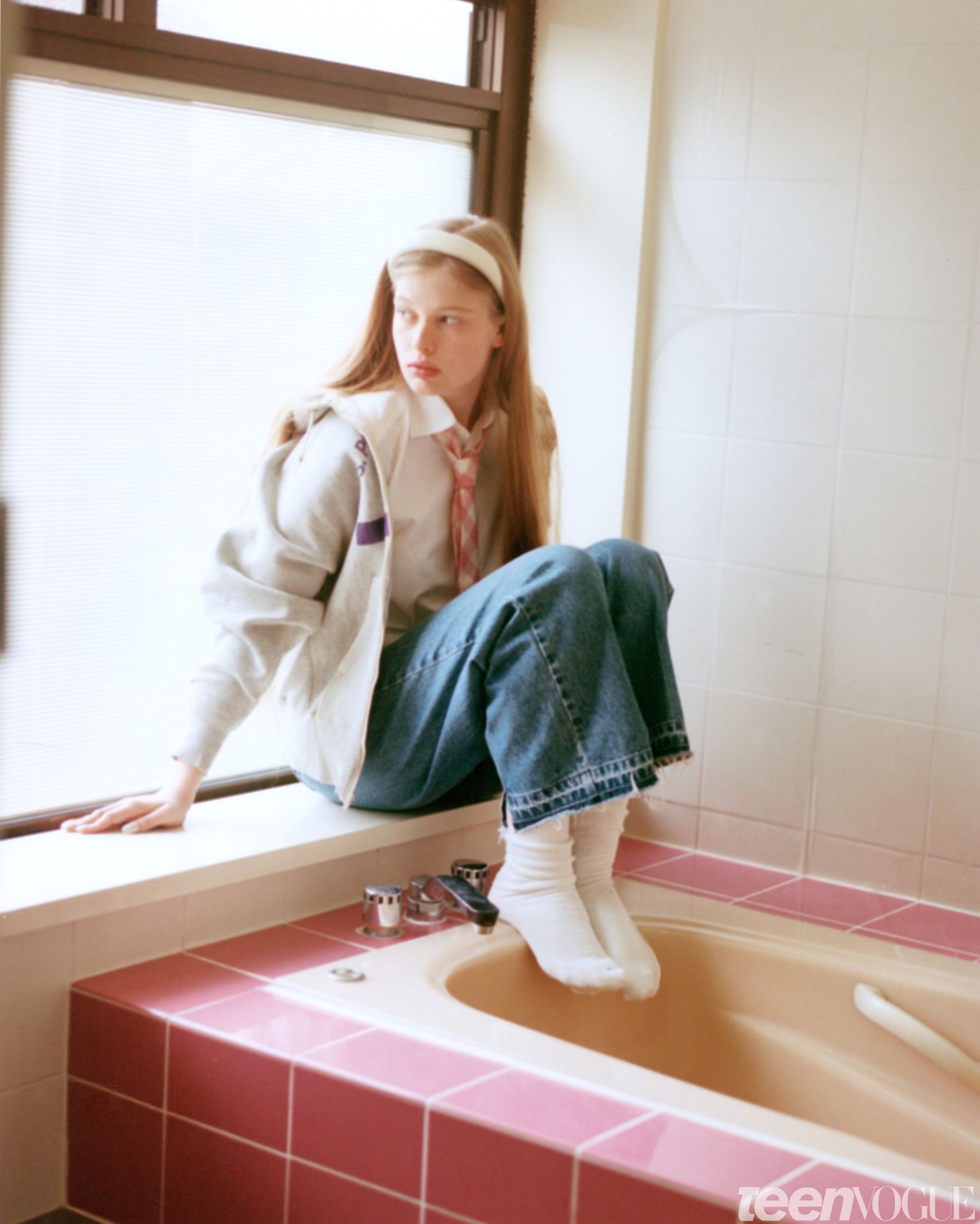 Vivian sits against a windowsill in a pastelcolored bathroom that matches the color palette of her outfit. She wears a...