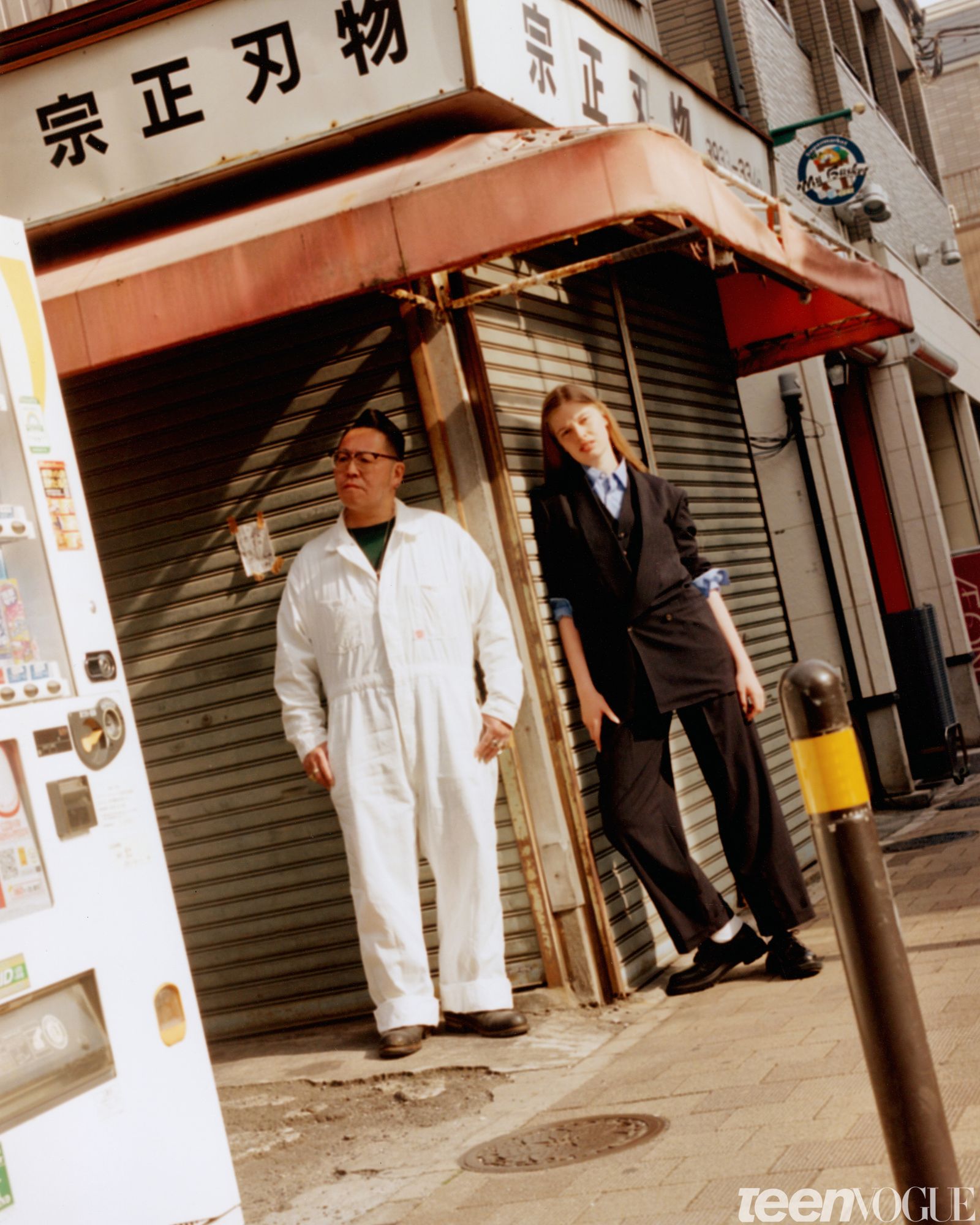 Vivian photographed leaning against a closed storefront outside in Tokyo wearing a matching jacket and pants.