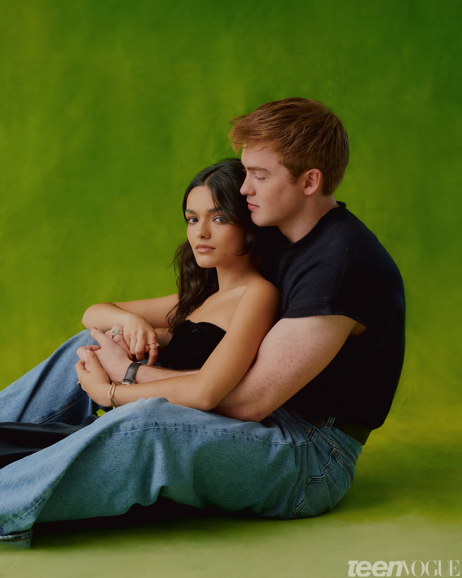 Rachel and Kit sitting against a green backdrop holding hands.