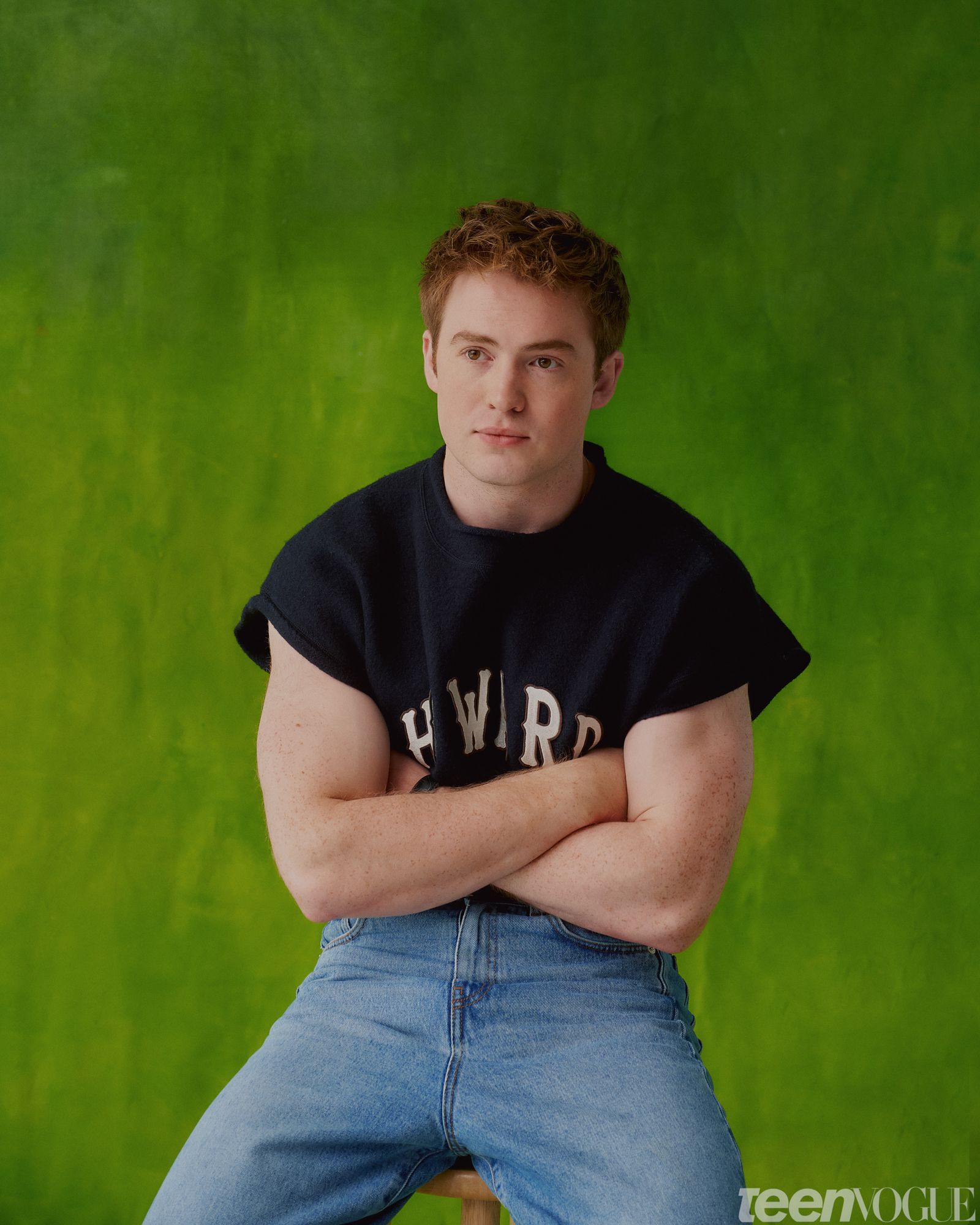 Kit hands crossed sitting on stool against a green backdrop.