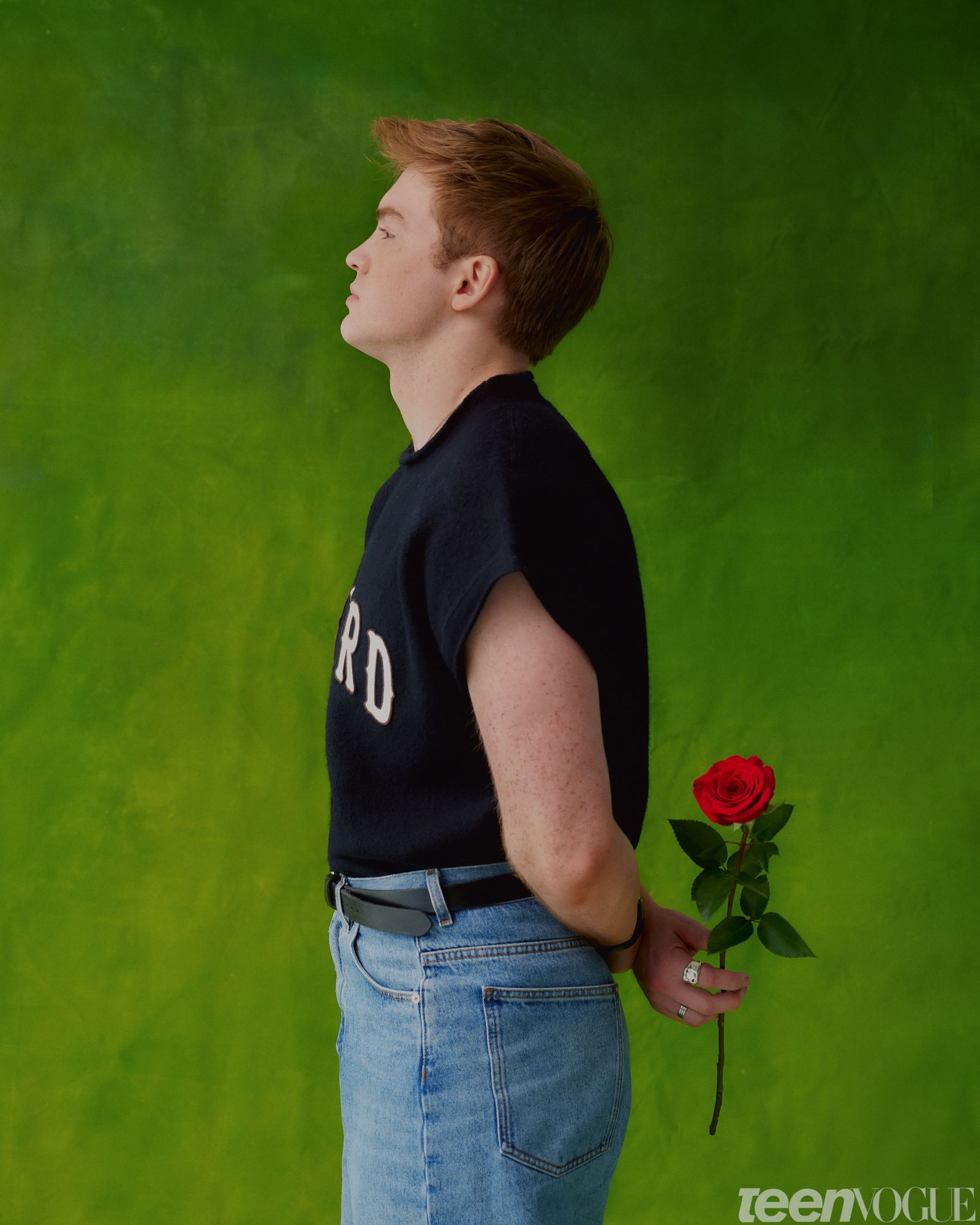 Profile of Kit holding a red rose wearing a navy sweatshirt black belt and jeans.